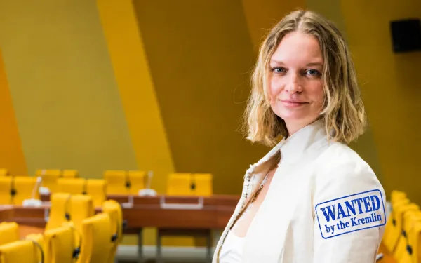 Ksenia Maximova in a lecture room, with a blue stamp reading Wanted by the Kremlin.